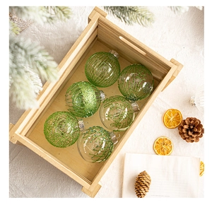 Detail of six clear glass Christmas balls with green glitter patterns in a wooden crate