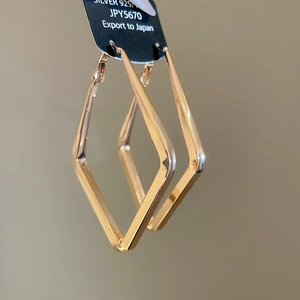 Close-up of golden geometric diamond-shaped earrings with 925 silver needle hallmark