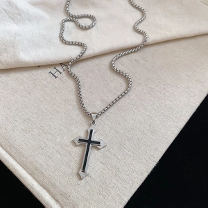 Close-up of a silver cross heart pendant with black enamel inlay on a beige linen bag