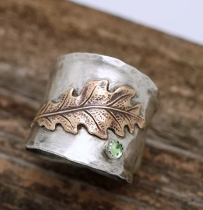 Macro shot of silver textured wide ring with bronze oak leaf and green gemstone detail
