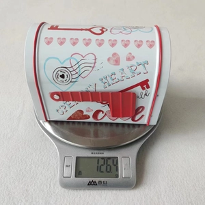 Macro view of white heart-patterned mailbox tin on a scale showing 126.4g weight