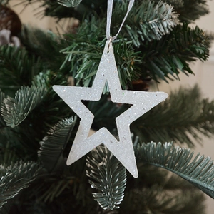 Sparkling silver glitter star ornament hanging on green Christmas tree branch with silk rope