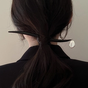 Detail of a minimalist black wooden hair stick with a white baroque pearl pendant
