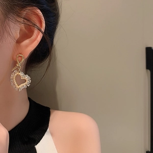 Close-up of heart-shaped gold earrings with embedded crystals and pearls on model