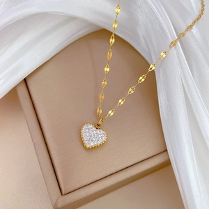 Detail of a gold heart pendant with white crystals on a luxury textured chain