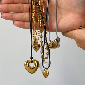 Close-up of heart pendants in gold, silver, and glass on various chains held by hand