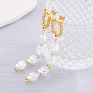 Détail macro de boucles d'oreilles géométriques en titane doré avec perles blanches élégantes