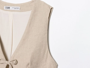 Detailed close-up of beige linen vest fabric texture and S-size brand neck label