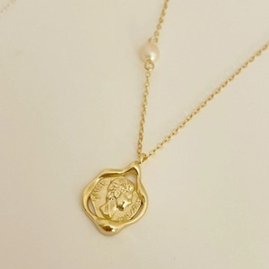 Close-up of a French vintage gold coin pendant necklace with a pearl detail and engraving