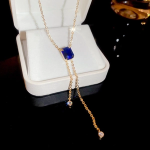 Detail of gold necklace featuring a rectangular blue stone and delicate dual tassels