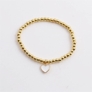 Detail of gold beaded stretch bracelet featuring a white enamel heart charm pendant