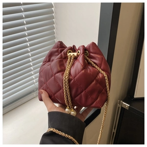 Detail of burgundy quilted bucket bag with gold chain strap and pearl drawstring ends