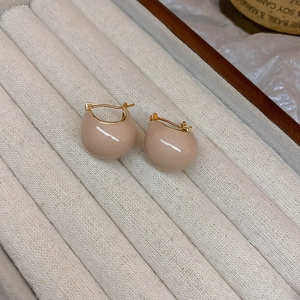 Macro view of gold-plated geometric bean earrings with cream enamel on beige velvet box