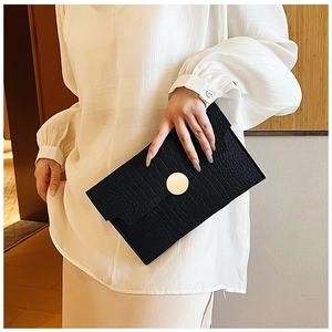 Detail of elegant black crocodile pattern envelope clutch with golden round buckle accent