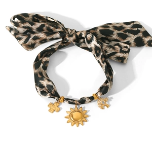 Detail of leopard print ribbon bracelet with sun, cross, and tree of life golden charms