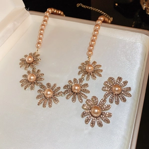 Detail view of champagne gold flower necklace with pearls and rhinestones in gift box