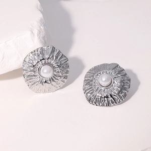 Detail of silver textured floral earrings with white pearls on a stone pedestal