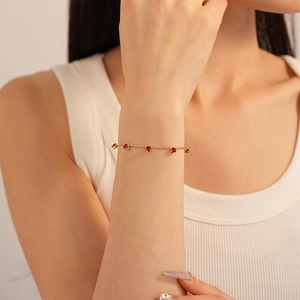 Gold beaded chain bracelet featuring five claw-set red round gemstones on a model wrist