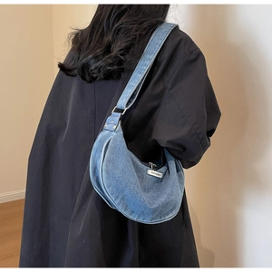 Side view of light blue denim crescent shoulder bag with wide strap on a model