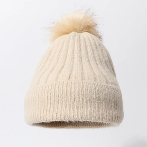 Close-up of beige ribbed knit beanie with a fluffy faux fur pompom and soft thick texture
