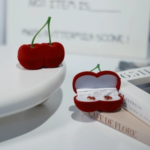 Primer plano de un joyero de terciopelo con forma de cereza roja sobre una mesa