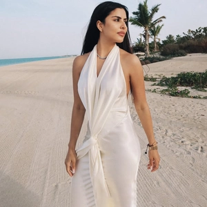 Détail de robe longue blanche en satin dos nu avec fente haute sur une plage ensoleillée
