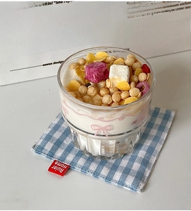 Detail of pink bow glass cup filled with yogurt and cereal on blue plaid coaster