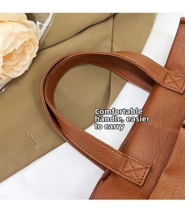 Detail of a brown leather tote with cross-stitched handles and a pebbled texture