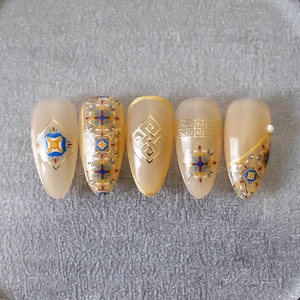 Ethnic style press-on nails with gold patterns and pearl accents on pink base