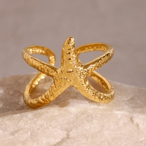 Detailed close-up of golden starfish ring with hammer-textured finish on natural stone