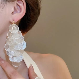Detailed view of layered round shell tassel earrings worn on ear for vacation style