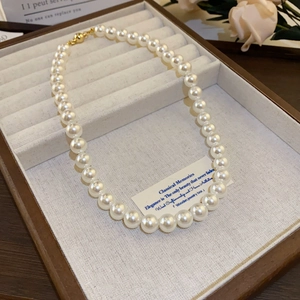 Detail of elegant white pearl necklace with golden clasp on beige jewelry tray