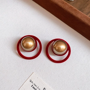 Detail of red flocked circular earrings with central gold metallic spheres on fabric