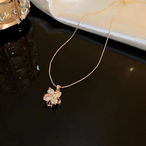 Close-up of golden four-leaf clover necklace with cubic zirconia on black mirror