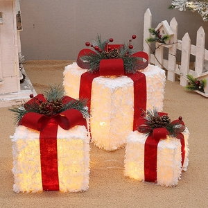 Close-up of white flocked Christmas gift box with red bow, pine cones and warm LED lights
