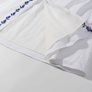 Detail of white cotton linen dress showing blue floral embroidery and inner lining