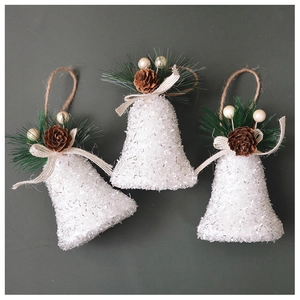 Détail de cloches de Noël blanches pailletées avec pommes de pin et aiguilles vertes