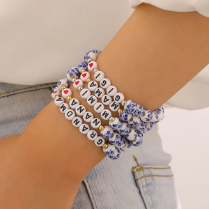 Dettaglio di braccialetti in ceramica blu a fiori con ciondoli a lettere impilati