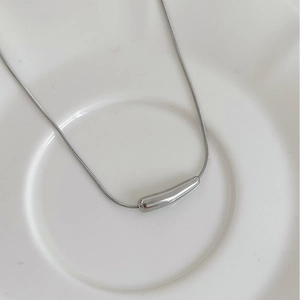 Dettaglio di una collana in argento con ciondolo a barra curva su un piatto di ceramica