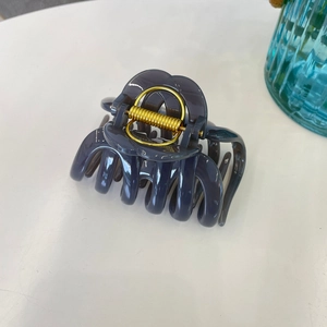 Top-down view of a large dark grey pumpkin hair claw clip with a strong golden metal spring