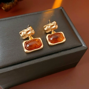 Vue macro de boucles d'oreilles carrées en résine ambre plaqué or sur boîte à bijoux