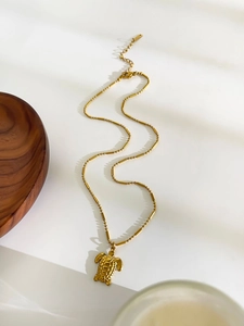 Detailed view of a gold sea turtle pendant on a unique beaded chain against white background