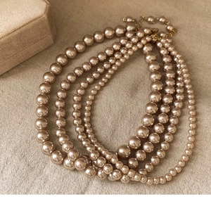 Detailed view of layered champagne pearl necklaces with gold metal clasps on textured fabric