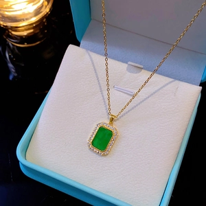 Close-up of golden necklace with green emerald pendant and zircons in jewelry box