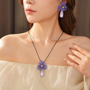 Detail shot of purple floral teardrop pendant necklace and earrings set on a model