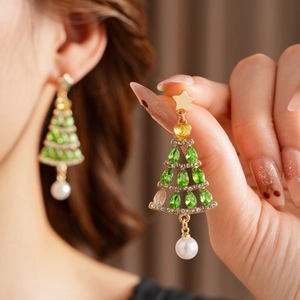 Close-up of gold Christmas tree earrings with green rhinestones and a hanging pearl