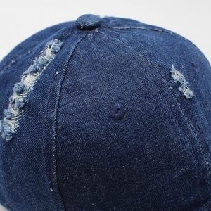 Dettaglio del cappellino da baseball in denim blu navy con fori consumati e bottone superiore