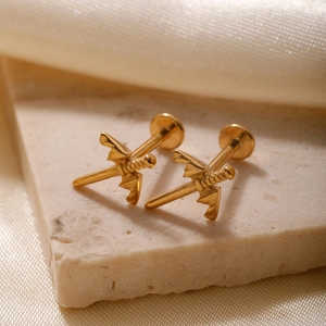 Golden dagger stud earrings with wings on beige stone and champagne silk background