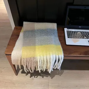 Detail view of a thick rainbow plaid scarf with yellow and grey tones and long fringes