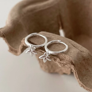 Detailed macro of S925 sterling silver leaf earrings resting on textured brown craft paper